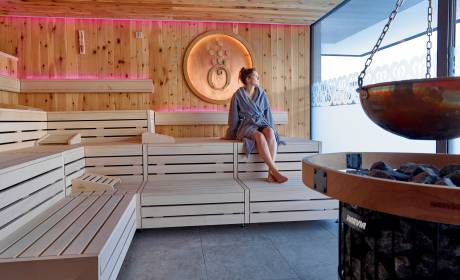  Frau mit Bademantel sitzt in Panorama Sauna