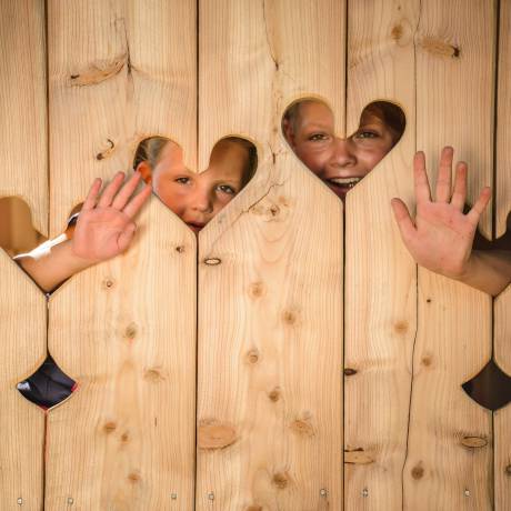Kinder hinter Holzwand mit Herzen winken hervor