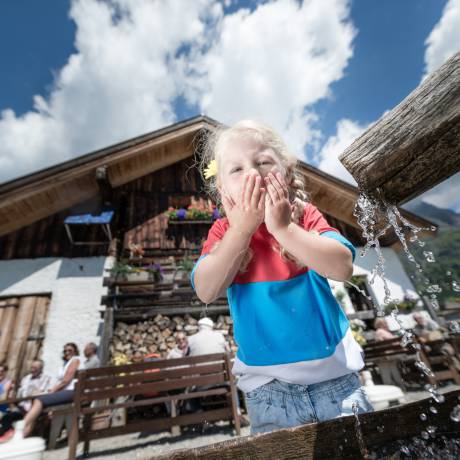 Kind trinkt aus Brunnen