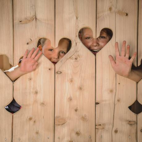 Children behind wooden wall with hearts waving out