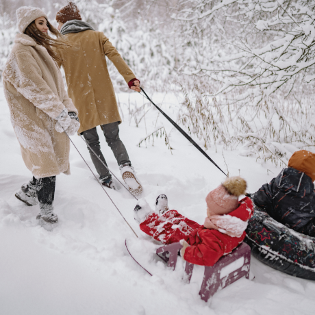 Parents pull the 2 children with the toboggans through the snowy mountains 