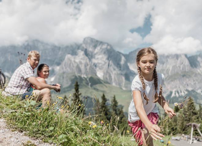 Mädchen pflückt ihren Eltern einen Strauß Blumen in den Bergen