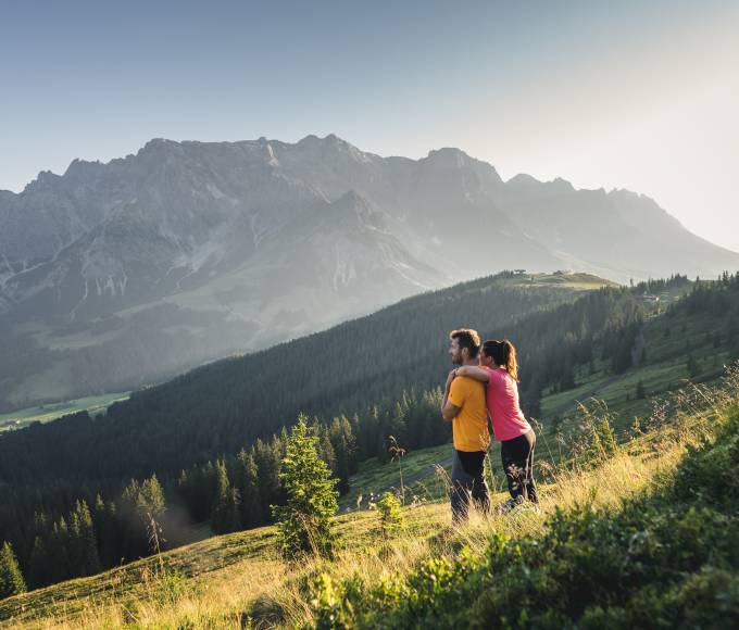 Frau umarmt Mann von hinten auf Bergwiese