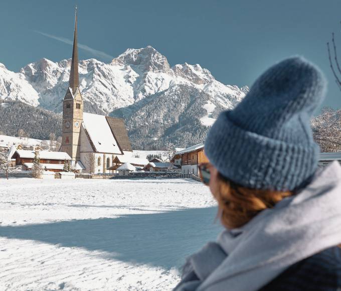 Woman in the snow with a view of the Maria Alm church tower and the mountains