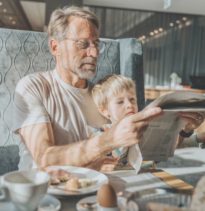 Vater und Sohn beim Frühstücken im Hotelrestaurant mit einer Zeitung