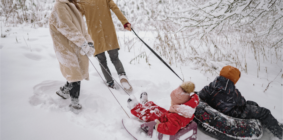 Parents pull the 2 children with the toboggans through the snowy mountains 