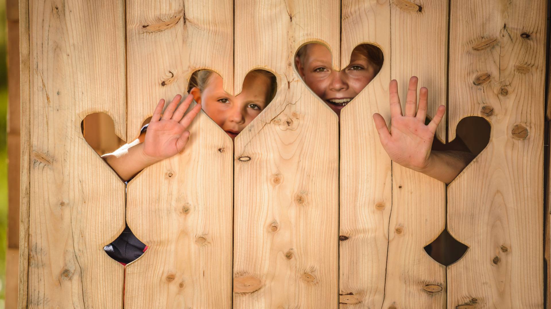 Kinder hinter Holzwand mit Herzen winken hervor