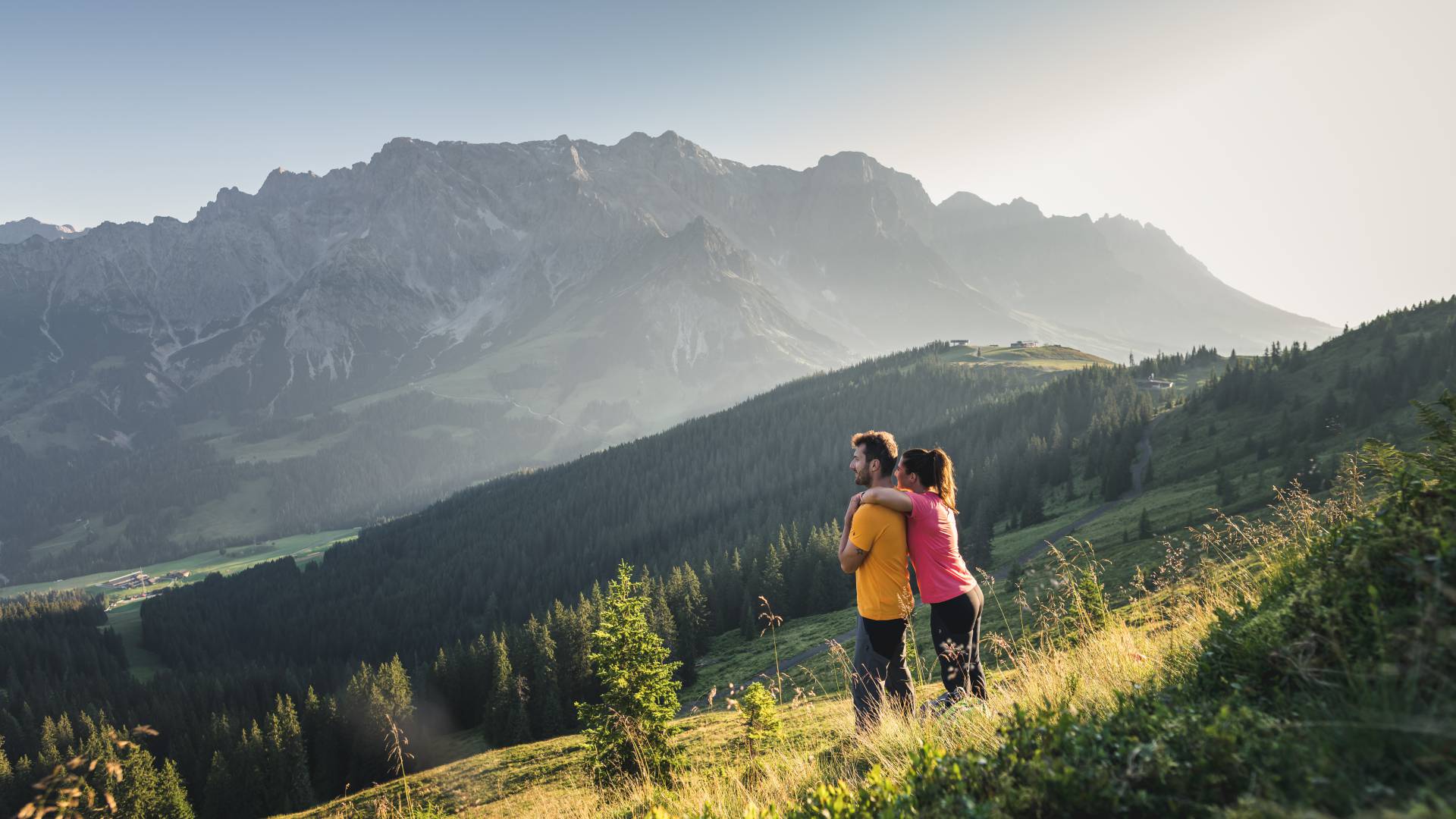 Frau umarmt Mann von hinten auf Bergwiese