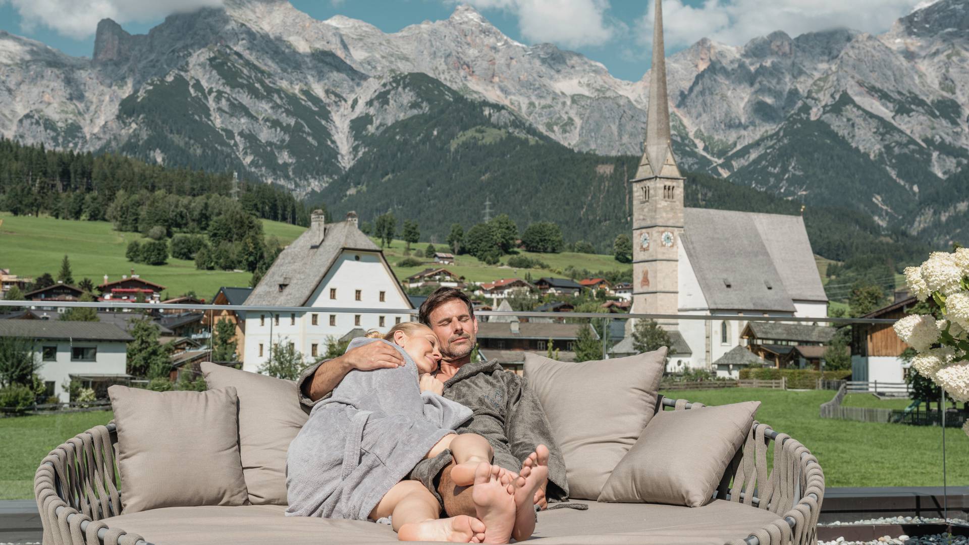 Couple on the sun deck with a view in summer at Hotel die HOCHKÖNIGIN in Maria Alm Wellness hotel Luxury hotel Family hotel
