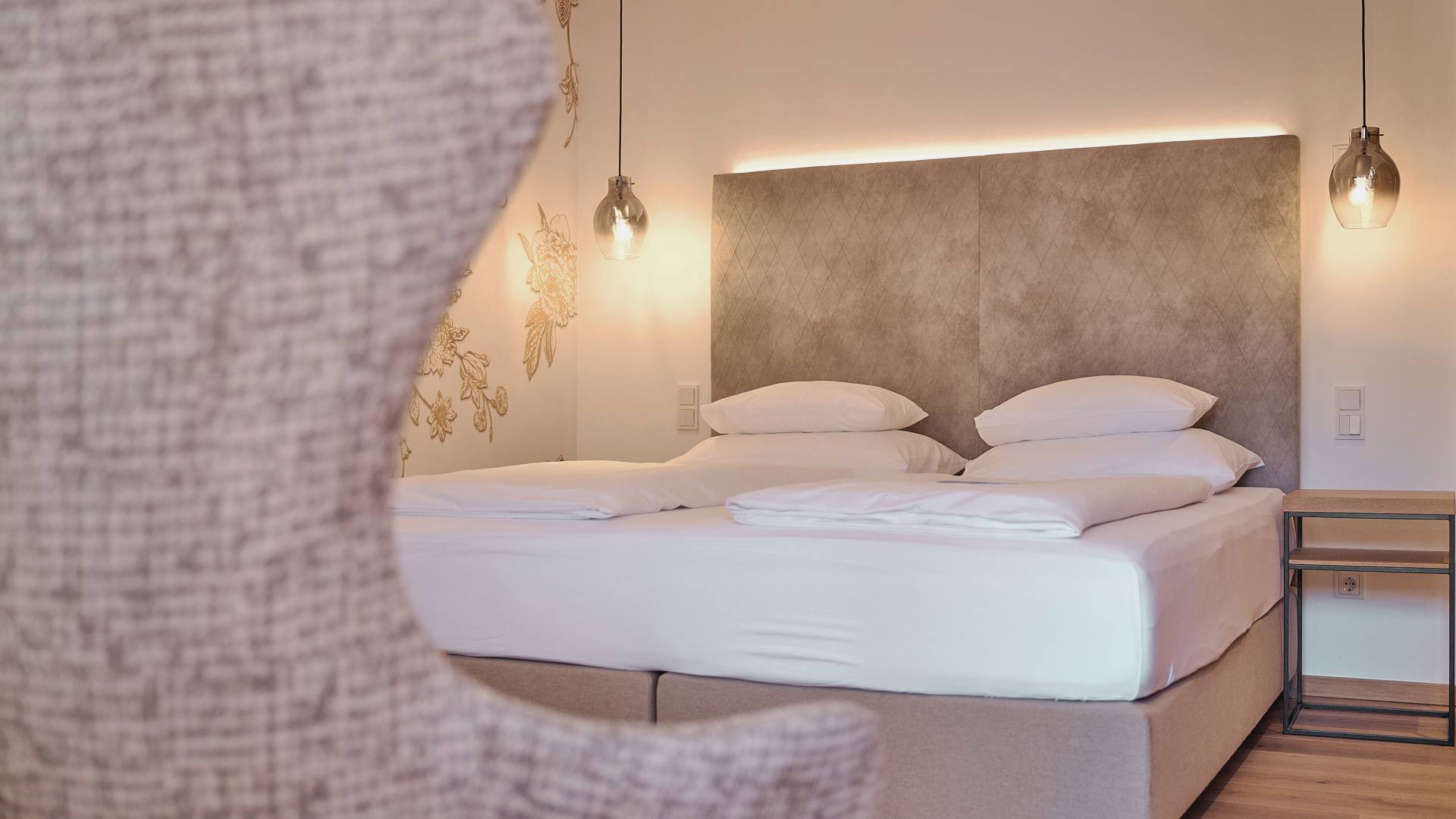 Bed in the hotel room of the HOCHKÖNIGIN with stylish lamps and noble wallpaper with golden flowers