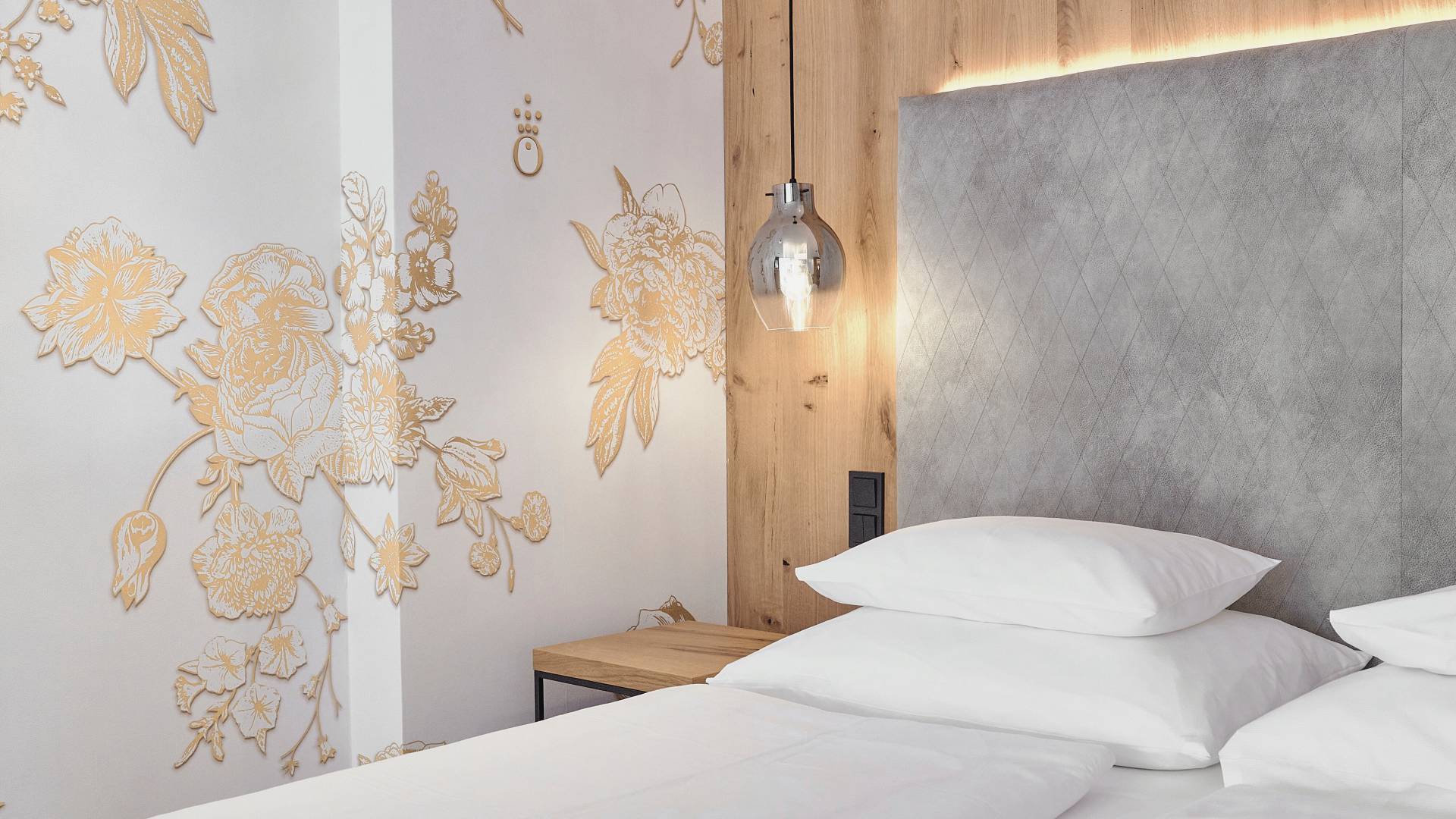 Bed in the hotel room of the HOCHKÖNIGIN with stylish lamps and noble wallpaper with golden flowers