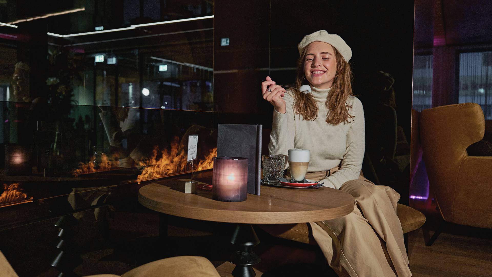 Woman in the lounge by the fireplace of the HOCHKÖNIGIN with a cafe latte