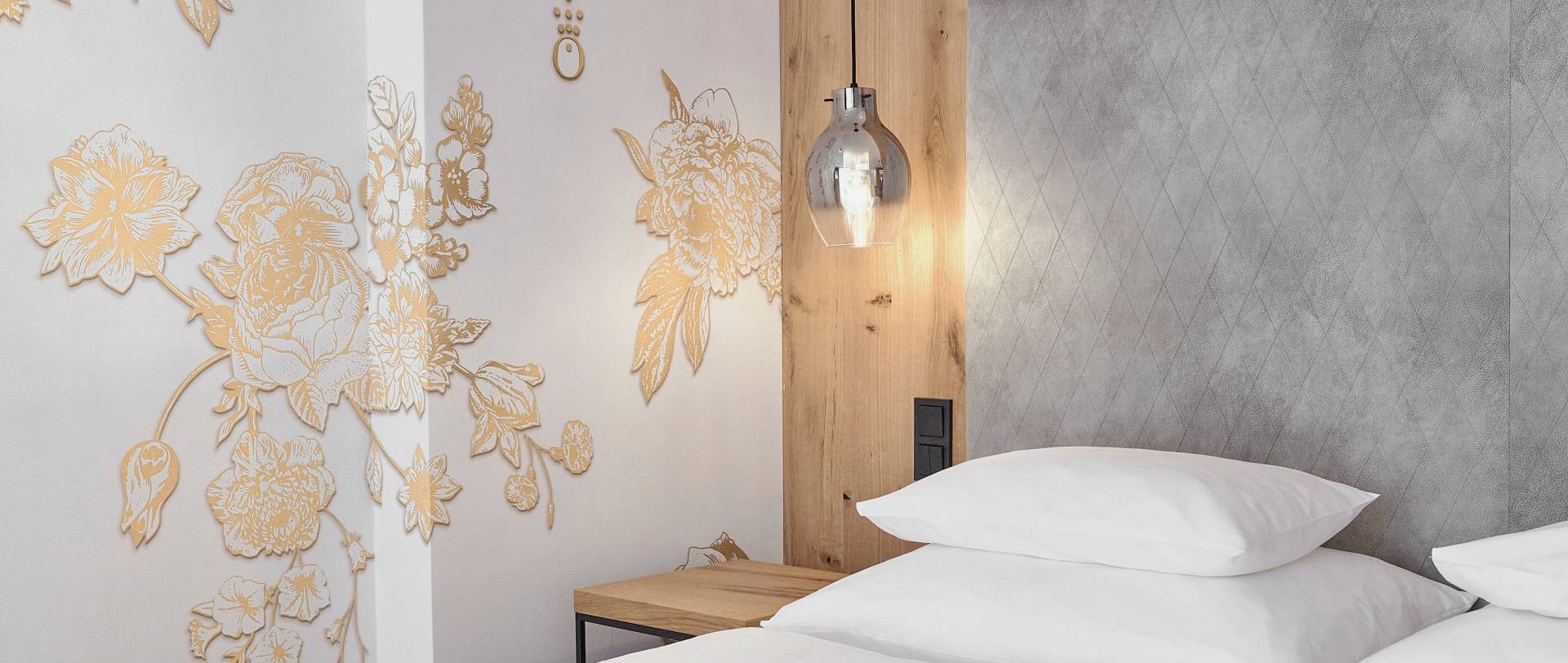 Bed in the hotel room of the HOCHKÖNIGIN with stylish lamps and noble wallpaper with golden flowers