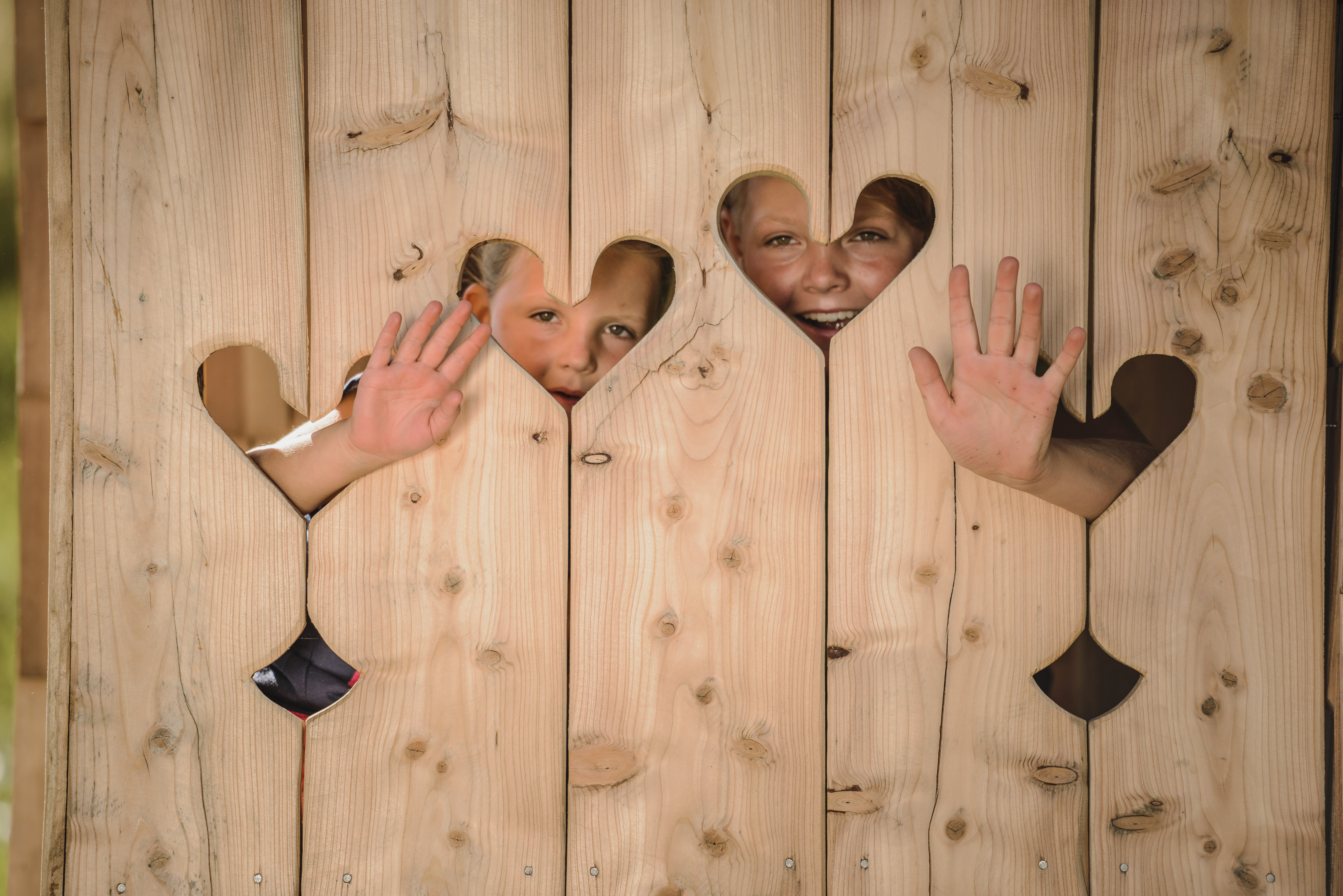 Children behind wooden wall with hearts waving out
